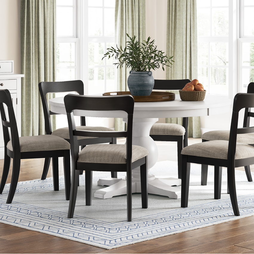 Dining room with a white table and dark wood chairs, light-colored walls, and large windows.